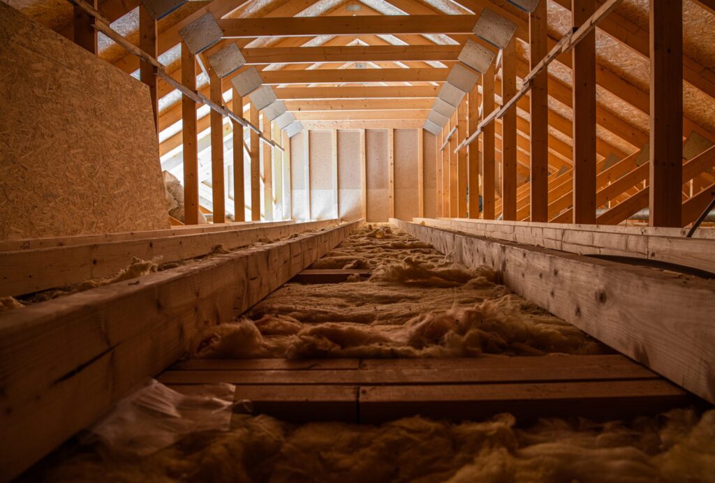 Attic interior with fiberglass insulation between the floor joists and open roof trusses above