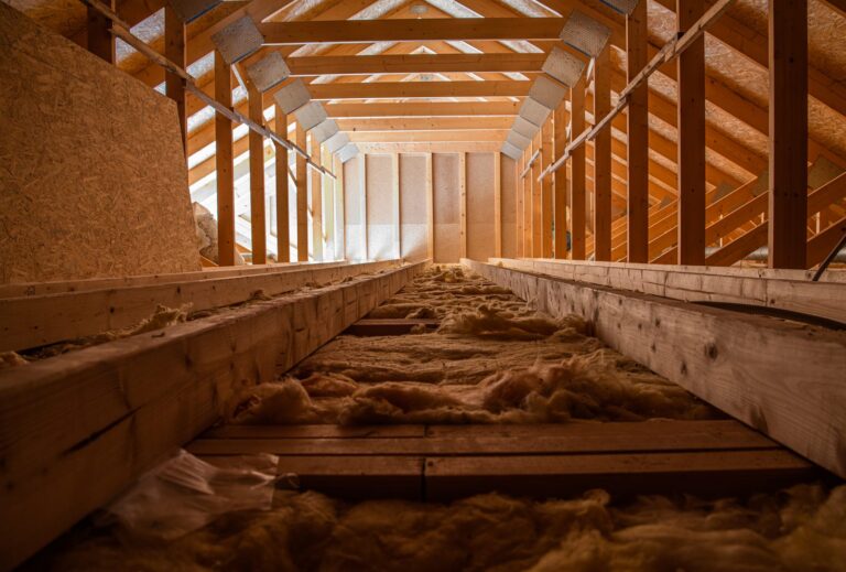 Attic interior with fiberglass insulation between the floor joists and open roof trusses above