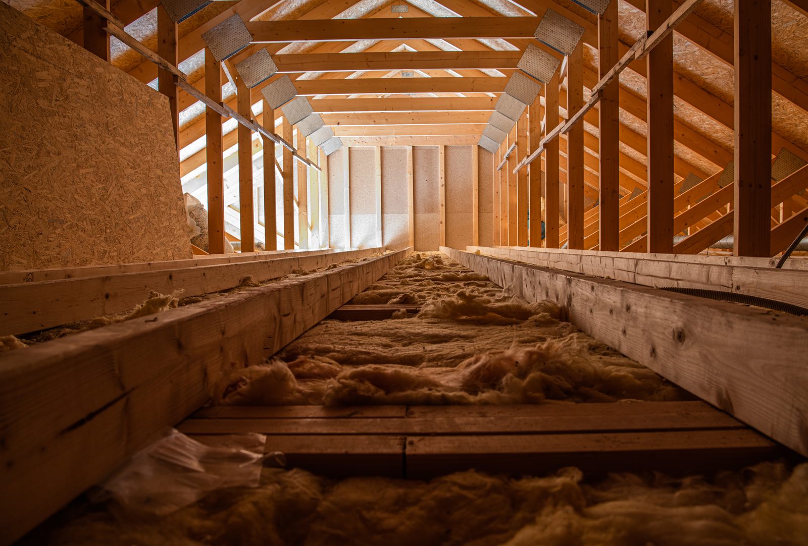Attic interior with fiberglass insulation between the floor joists and open roof trusses above