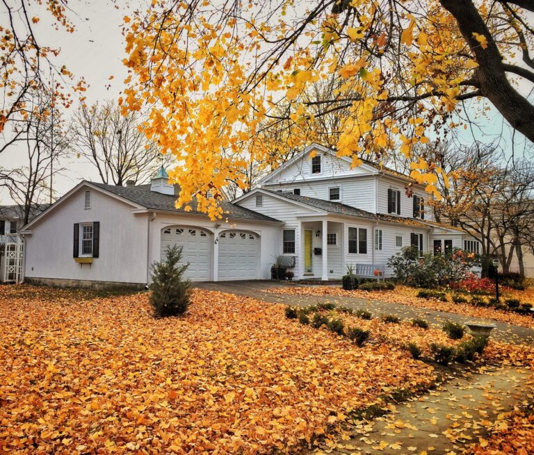 White colonial home with an asphalt shingle roof surrounded by fallen autumn leaves