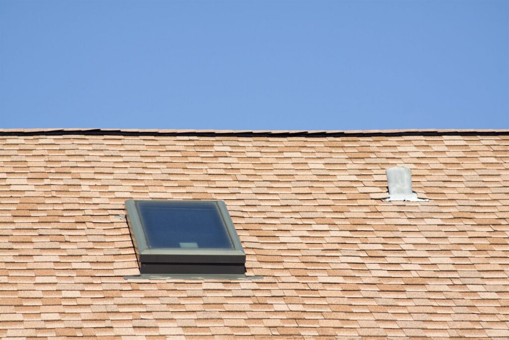 Skylight and plumbing vent flashing on an asphalt shingle roof against a blue sky